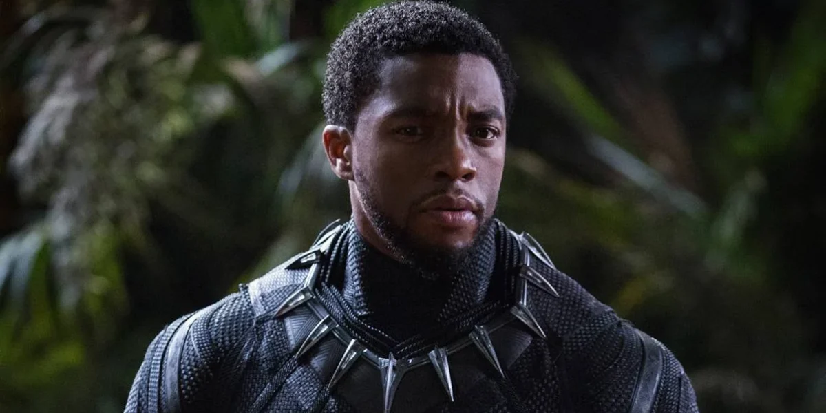 Chadwick Boseman no papel de T'Challa em "Pantera Negra" (2018). Há uma mata desfocada ao fundo e o autor está nos trajes do super-herói, sem apenas a parte da cabeça.