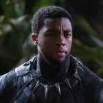 Chadwick Boseman no papel de T'Challa em "Pantera Negra" (2018). Há uma mata desfocada ao fundo e o autor está nos trajes do super-herói, sem apenas a parte da cabeça.