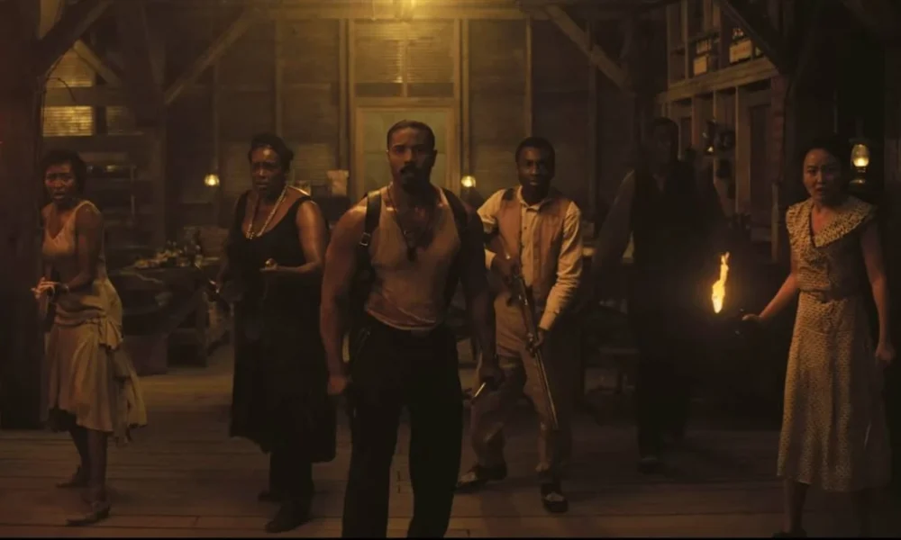 Elenco de Sinners interpretando seus personagens no lonca de terror de vampiros. Os personagens estão caracterizados com roupas da década de 30 em um casebre na Louisiana. Michael Jordan está ao centro, todos estão com semblante assustado e armados.