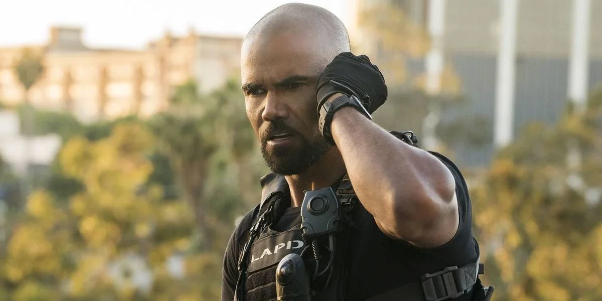 Shemar Moore como Daniel 'Hondo' Harrelson, protagonista de "S.W.A.T.". Fardado, ele coloca a mão na escuta no ouvido esquerdo e tenta prestar atenção. No fundo desfocado, árvores meio a uma cidade.