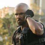 Shemar Moore como Daniel 'Hondo' Harrelson, protagonista de "S.W.A.T.". Fardado, ele coloca a mão na escuta no ouvido esquerdo e tenta prestar atenção. No fundo desfocado, árvores meio a uma cidade.