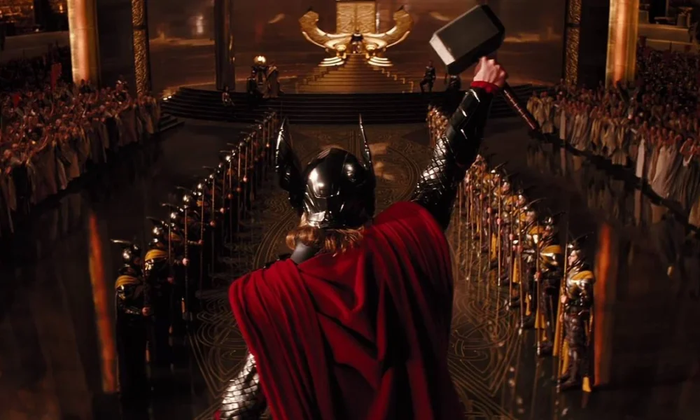 Thor erguendo seu martelo em "Thor" (2011), centraliado na tela e com capacete de Asgard e capa vermelha.