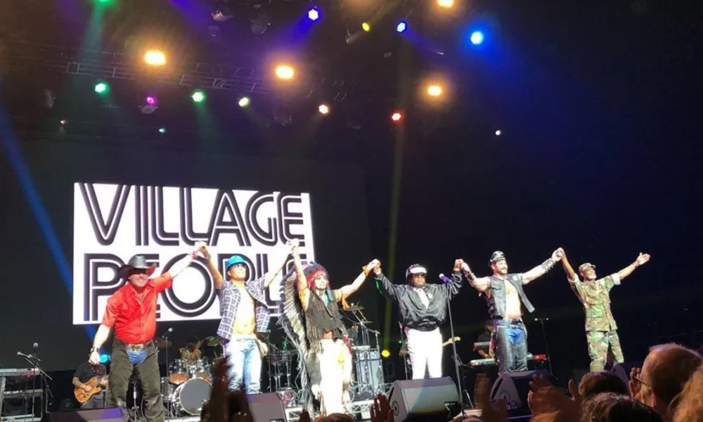 Village People em Adelaide, 2019, para show da turnê Summer Series Tour. Membros do grupo estão de mãos dadas e braços levantados em frente ao palco.