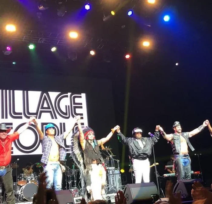Village People em Adelaide, 2019, para show da turnê Summer Series Tour. Membros do grupo estão de mãos dadas e braços levantados em frente ao palco.