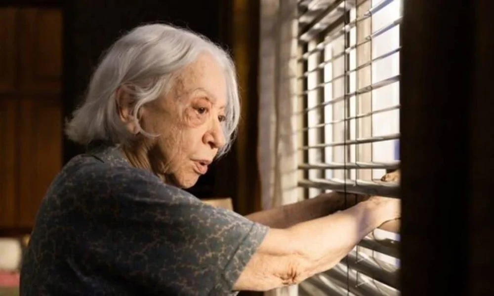 Fernanda Montenegro como a protagonista de "Vitória" (2025), Dona Nina/Vitória, na janela de sua casa observando a movimentação na rua.