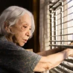 Fernanda Montenegro como a protagonista de "Vitória" (2025), Dona Nina/Vitória, na janela de sua casa observando a movimentação na rua.