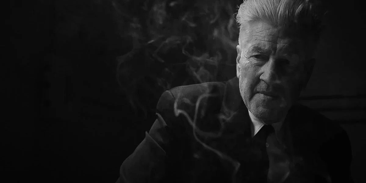 David Lynch, Diretor Lendário de “Twin Peaks”‘ e “Cidade dos Sonhos”, Morre aos 78 Anos David Lynch em material promocional de "What Did Jack Do?", curta de 2017 em preto e branco. Ele está de terno e podemos ver uma fumaça de cigarro em volta de seu corpo.