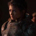 Oscar 2025 | “Ainda Estou Aqui” Segue na Disputa Pela Indicação na Categoria “Melhor Filme Internacional” Zendaya como Chani em "Duna: Parte 2" (2024), pela Warner Bros. Personagem está com um semblante sério, olhando fixamente a um ponto. Seus olhos azuis são destaque na imagem dominada por tons escuros.