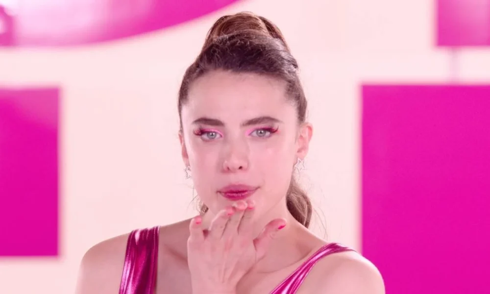 Margaret Qualley como a protagonista de "A Substância" (2024). Ela está com roupas de ginástia rosa, delineado rosa, unhas também rosa, olhando para a câmera e assoprando um beijinho.