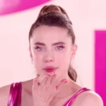 Margaret Qualley como a protagonista de "A Substância" (2024). Ela está com roupas de ginástia rosa, delineado rosa, unhas também rosa, olhando para a câmera e assoprando um beijinho.