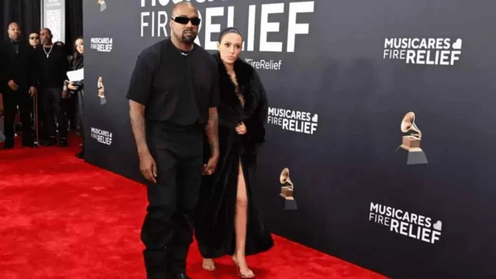 Bianca Censori: Quem é a Peladona do Grammy 2025? 1 Artista de joias e esposa de Kanye West, Bianca Censori, desfilando no Grammy. Ela está com um vestido completamente transparente, mas nessa imagem ela ainda está coberta com um longo vestido preto de pelos.