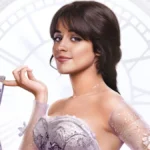Camila Cabello em imagem promocional como a protagonista de "Cinderella" (2021). Ela segura o sapato de cristal com um dos dedos e sorri para a câmera.