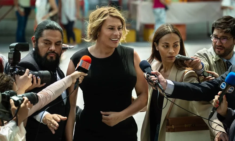 Protagonista homônima de "Emilia Pérez" dando entrevista durante o longa, ao lado de sua acessora, interpretada por Zoe Saldaña.