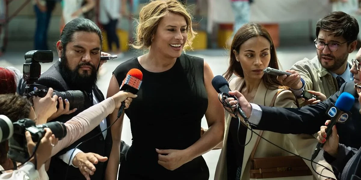 Protagonista homônima de "Emilia Pérez" dando entrevista durante o longa, ao lado de sua acessora, interpretada por Zoe Saldaña.