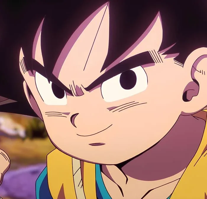 Câmera focada no rosto de Goku, com ele com um sorriso e em posição de luta. Ele está transformado em criança. Imagem da série "Dragon Ball Daima".