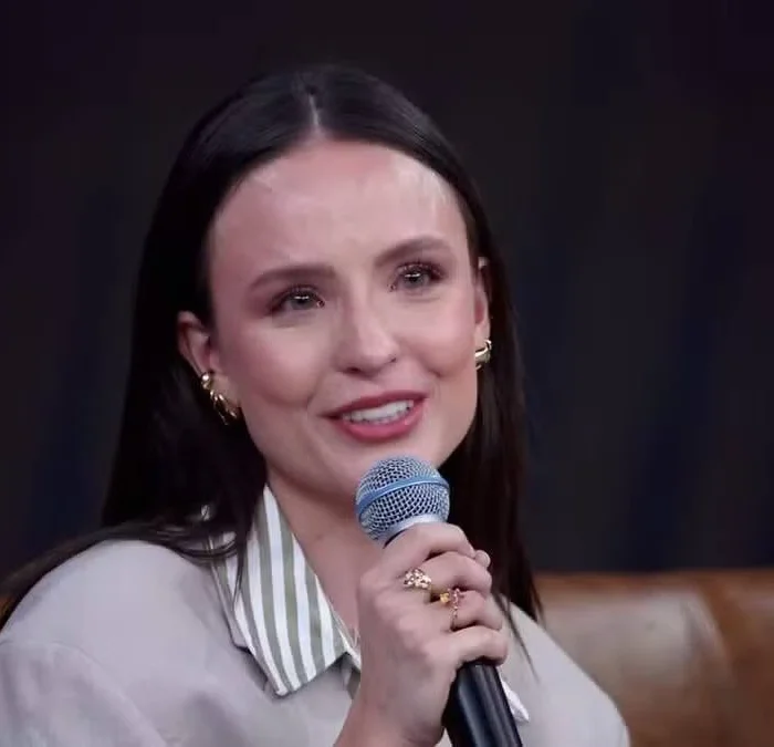 Atriz Larissa Manoela emocionada, com um microfone ma mão direita, olhos lacrimejando, cabelo solto, e uma camisa branca. Atriz está no "Domingão". No canto superior esquerdo há a hashtag do programa e no inferior direito o logo da TV Globo.
