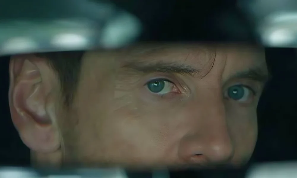 Michael Fassbender como Brandon Colby em "A Agência". Vemos seu rosto olhando através deu uma fresta horizontal.