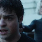 Noah Centineo como o protagonista de "O Recruta", na temporada 2, com uma arma apontada até ele por uma mulher loira.