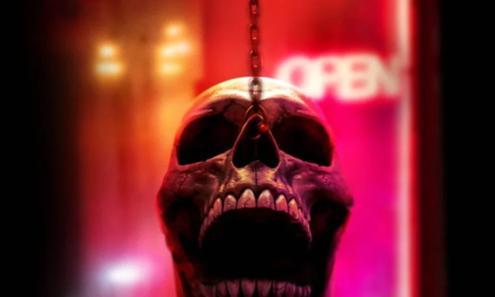 Uma caveira com uma corrente segurando-na pelo nariz, ela está com a boca aberta como se gritasse. Atrás dela há luzes neon e a palavra "on" em um letreiro de bar.