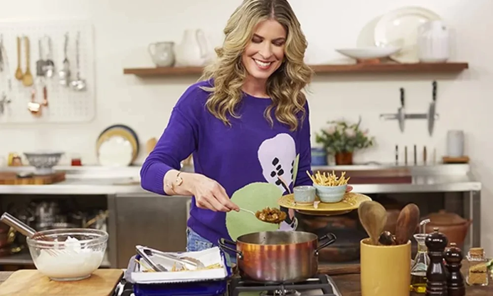 Rita Lobo em uma cozinha cheia, com uma blusa roxa, sorrindo, apresentando o "Cozinha Prática", do GNT.