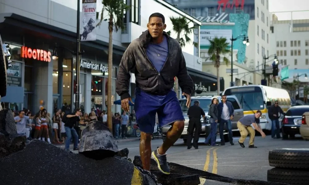 Will Smith flutuando como o herói protagonista de "Hancock" (2008), na rua, com o asfalto estourado ao fundo fruto de um confronto.