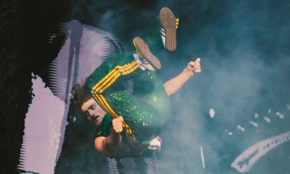 Benson Boone em meio a salto mortal no seu show no Lollapalooza Brasil 2025. Ele está usando roupas com as cores da bandeira do Brasil.