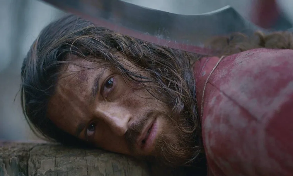 Can Yaman como o protagonista da série "O Turco". Ele possui uma arma sob sua cabeça e está prestes a ser atacado.