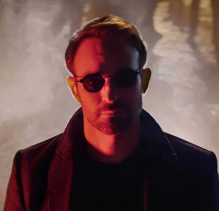 Protagonista de "Demolidor: Renascido" no primeiro episódio. Atrás dele uma explosão. Ele está de óculos e na sua cara há um filtro vermelho.