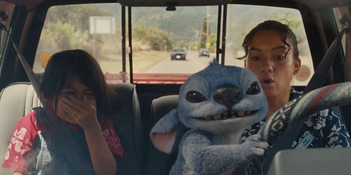 Lilo à esquerda, rindo, e Nani, à direita, preocupada, no volante, mas observando o alien Stitch dirigir o carro. Imagem do live-action de 2025 "Lilo & Stitch".