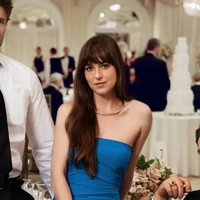 Chris Evans, em pé à esquerda, Dakota Johnson, sentada apoiada na mesa, e Pedro Pascal, direita, sentado de pernas cruzadas. Os três atores posam de forma enigmática para a câmera, trajados de gala e com um casamento ao fundo. Imagem do filme "Materialists", da A24.