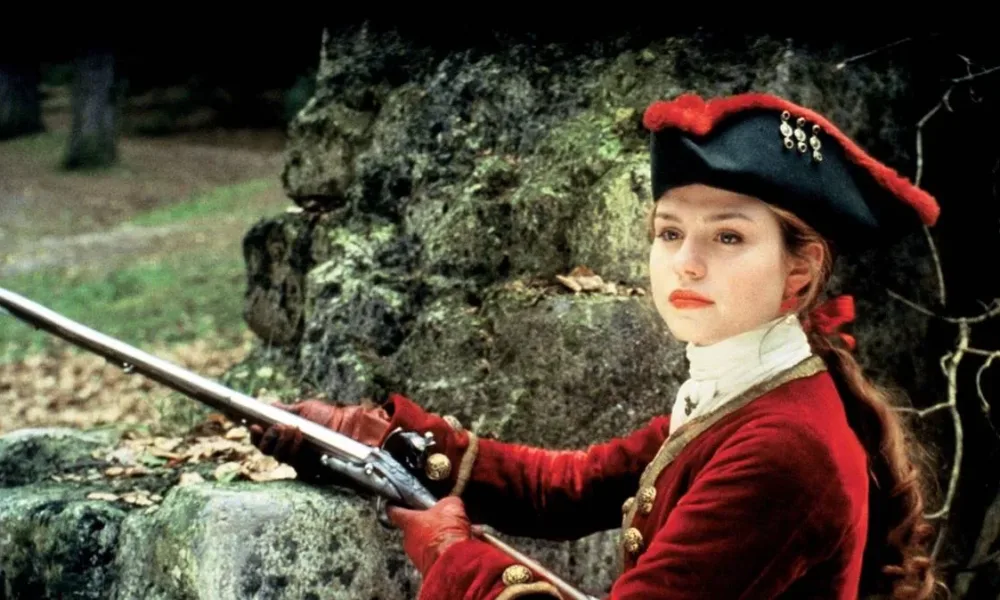 Émilie Dequenne vestida com roupas vermelhas do século XVIII e empunhando uma arma. Imagem do filme "O Pacto dos Lobos".