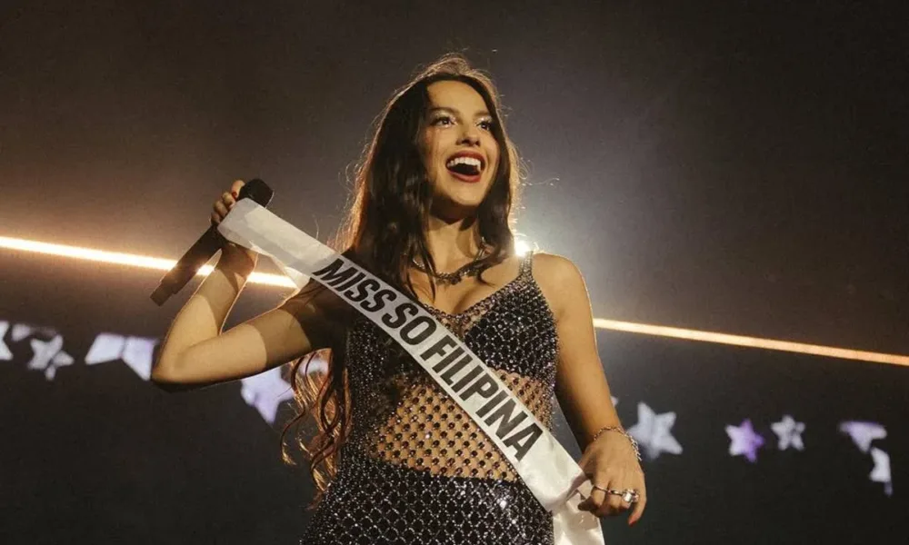 Olivia Rodrigo em show em Manila, 2024, com uma faixa "Miss So Filipina" em maiúsculo, e um sorriso no rosto.
