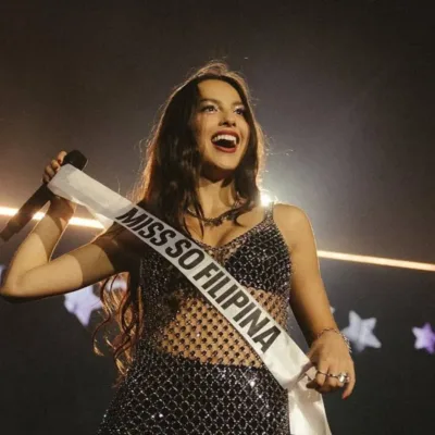 Olivia Rodrigo em show em Manila, 2024, com uma faixa "Miss So Filipina" em maiúsculo, e um sorriso no rosto.