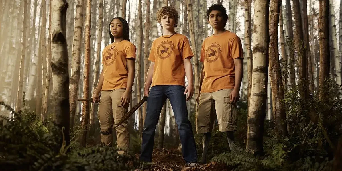 Percy Jackson e os Olimpianos | Série Retorna Com Trailer Para 2ª Temporada Annabeth, Percy, Grover, da série "Percy Jackson e os Olimpianos" em um bosque da série. Eles estão com o uniforme do acampamento e Percy está empunhando uma espada.