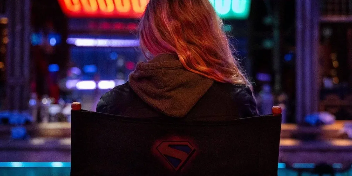 Atriz Milly Alcock sentada em uma cadeira de estúdio de gravações de cinema, de costas. Ela está em destaque e o fundo, a sua frente, está desfocado, e está com uma estética neon e cyberpunk vibrante.