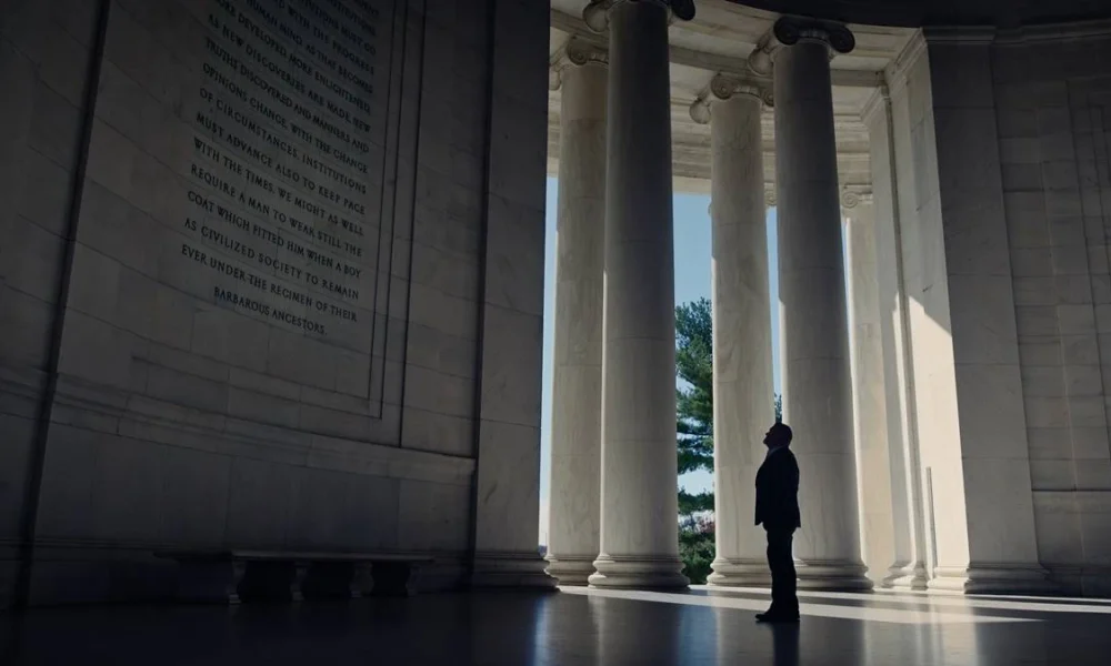 Homem de terno, enquadrado à grandiosidade de um monumento de mármore com escritos em inglês. Imagem do documentário "The Age of Disclosure".