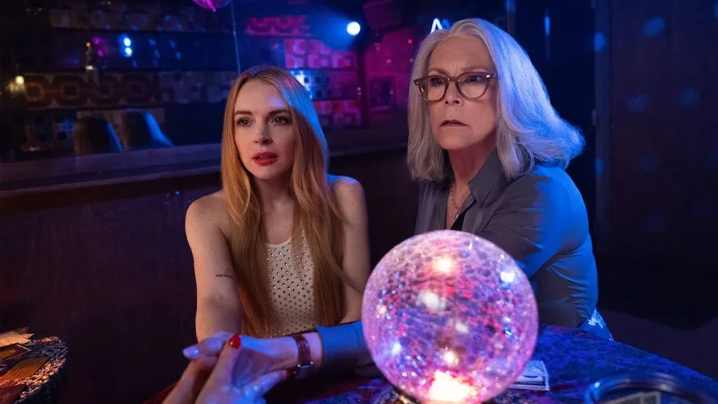 Uma Sexta-feira Mais Louca Ainda | Confira Trailer da Sequência de "Freaky Friday" (2003) 1 Lindsay Lohan, esquerda, e Jamie Lee Curtis, direita, como as protagonistas de "Uma Sexta Feira Mais Louca Ainda". Elas estão com as mãos apoiadas em uma mesa e as mostrando para uma vidente. Há uma bola de cristal em destaque no plano à direita, e há luzes neon em um ambiente um tanto escuro.