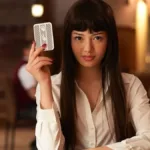 Protagonista de 'BET', adaptação live-action de "Kakegurui". Protagonista está com a mão esquerda na mesa, cotovelo direito apoiado e segurando uma carta com a mão direita, encarando o espectador, vestindo uma camisa branca.