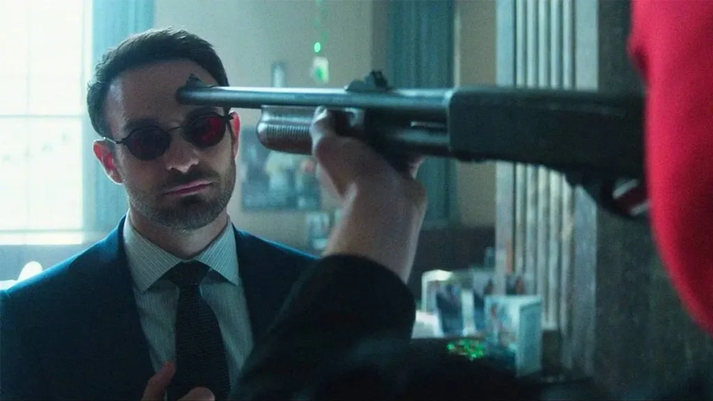 Demolidor: Renascido | A Volta da Série do Homem Sem Medo Pelo Disney+ 1 O Demolidor tendo a ele uma arma apontada à cabeça por um assaltante de banco, mantendo o herói uma expressão neutra. Imagem do 5º episódio da primeira temporada de "Demolidor: Renascido".