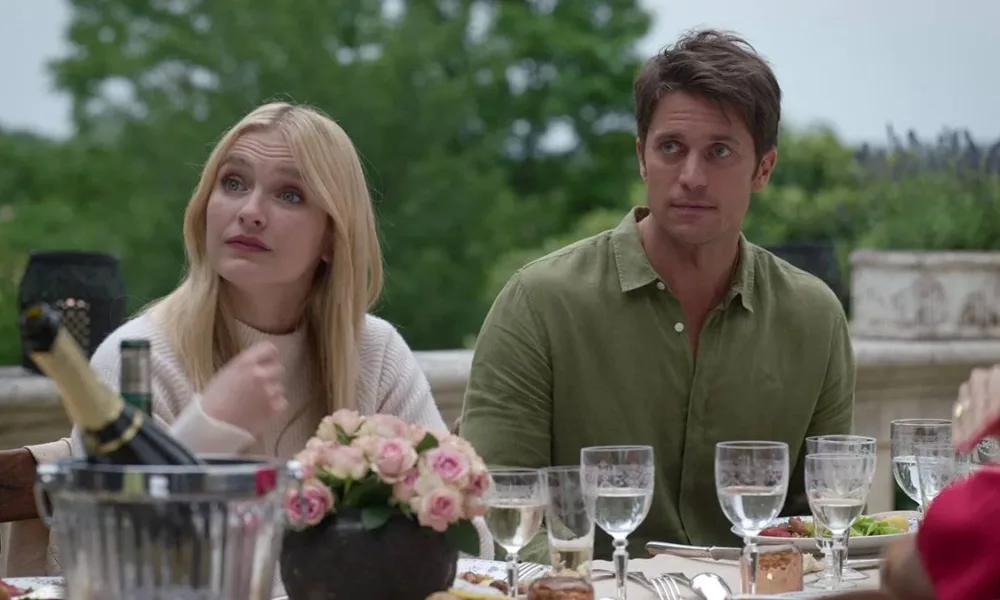 Lucas Bravo a direita da imagem sentado em uma mesa ao ar livre. Ator fez críticas a própria série "Emily in Paris". Imagem do oitavo episódio da segunda temporada.