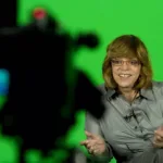 Missão Impossível 8 | Veja o trailer do último filme da franquia Gloria Perez em 2011 sentada em uma poltrona para dar uma entrevista. Ela sorri e gesticula. Atrás dela há uma tela verde e a sua frente, desfocada, um equipamento de câmera.
