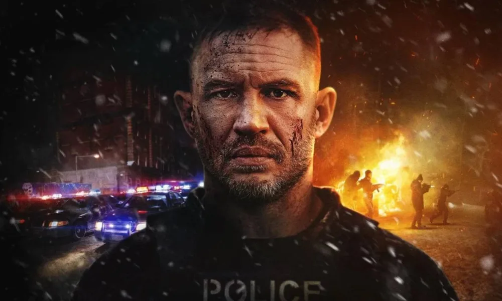 Protagonista do drama de ação "Havoc" (2025), pela Netflix. Cinzas caem pela tela e há um incêndio ao fundo. Ele faz uma cara séria, com um olhar profundo, quase chocado, mas ainda muito sério.