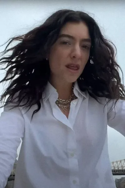 Cantora Lorde com uma camisa branca e colar em corrente de ouro com cabelos ao vento, roupa molhada, e câmera capturando-a sutilmente de um ângulo inferior, no clipe de "What Was That".