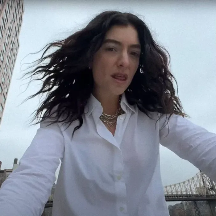 Cantora Lorde com uma camisa branca e colar em corrente de ouro com cabelos ao vento, roupa molhada, e câmera capturando-a sutilmente de um ângulo inferior, no clipe de "What Was That".