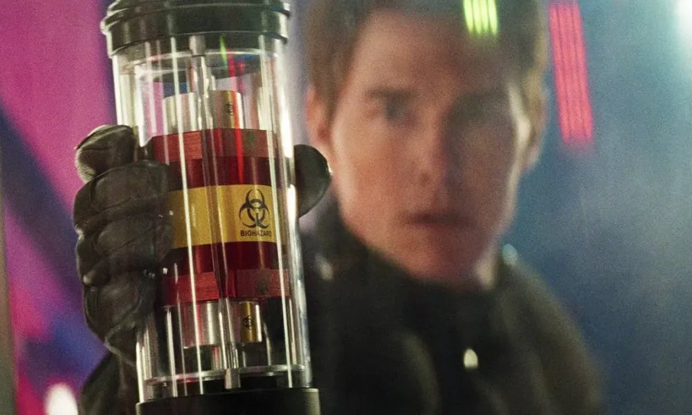 Tom Cruise segurando um frasco de "biohazard" focado. Seu rosto aparece desfocado junto ao cenário. Imagem do oitavo filme da franquia "Missão Impossível".