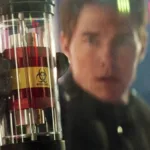 Tom Cruise segurando um frasco de "biohazard" focado. Seu rosto aparece desfocado junto ao cenário. Imagem do oitavo filme da franquia "Missão Impossível".