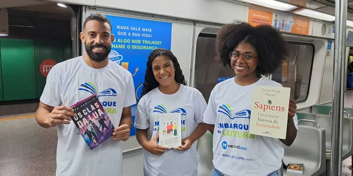 “Embarque na Leitura” | Bienal do Livro Rio Distribuiu 2,5 Mil Livros nos Trens do MetrôRio Três pesssoas com camisetas da iniciativa "Embarque na Leitura" em 2025, distribuindo livros no MetrôRio. Cada uma segura um livro, em ordem: "Os clãs da lua", "Mentirosos", e "Sapiens: uma breve história da humanidade".