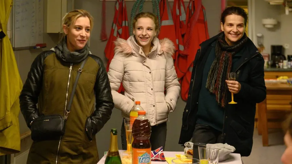 Entre Dois Mundos | O Discreto Interesse Burguês Pela Limpeza de Privadas 1 Elenco do filme francês "Entre Dois Mundos" (2022) em uma cena com roda de confraternização entre as trabalhadoras do longa. Elas estão em torno de uma mesa com quitutes baratos.
