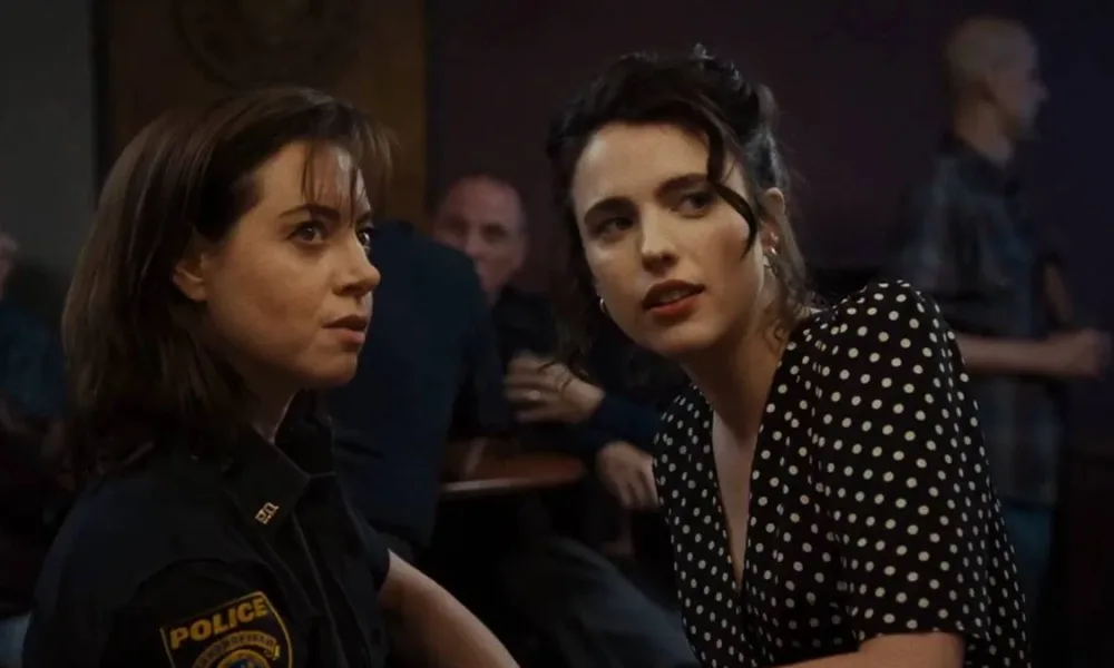 Aubrey Plaza e Margaret Qualley como personagens de "Honey Don't!", olhando para algo/alguém em um ponto longe da câmera, uma inclinada para a outra.