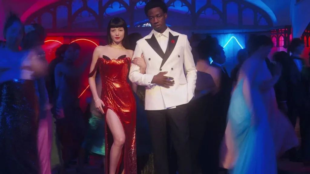 Kakegurui: Bet | Adaptação Plastificada, Mas Mantém Bom Humor Dentro do Possível Para Temporada 1 2 Yumeko (esquerda), vestido vermelho, e Ryan (direita), smoking branco, de braços dados posando para uma foto do baile em "Kakegurui: Bet".